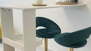 Una mesa blanca con superficie de vidrio y dos sillas color turquesa con patas doradas.