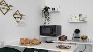 Una cocina moderna con muebles blancos, un microondas negro y una cafetera. Hay dos taburetes verdes y una planta en la encimera.