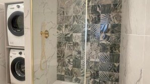 Un baño con lavadora, ducha con puerta de vidrio y pared de azulejos con diseño de hojas.