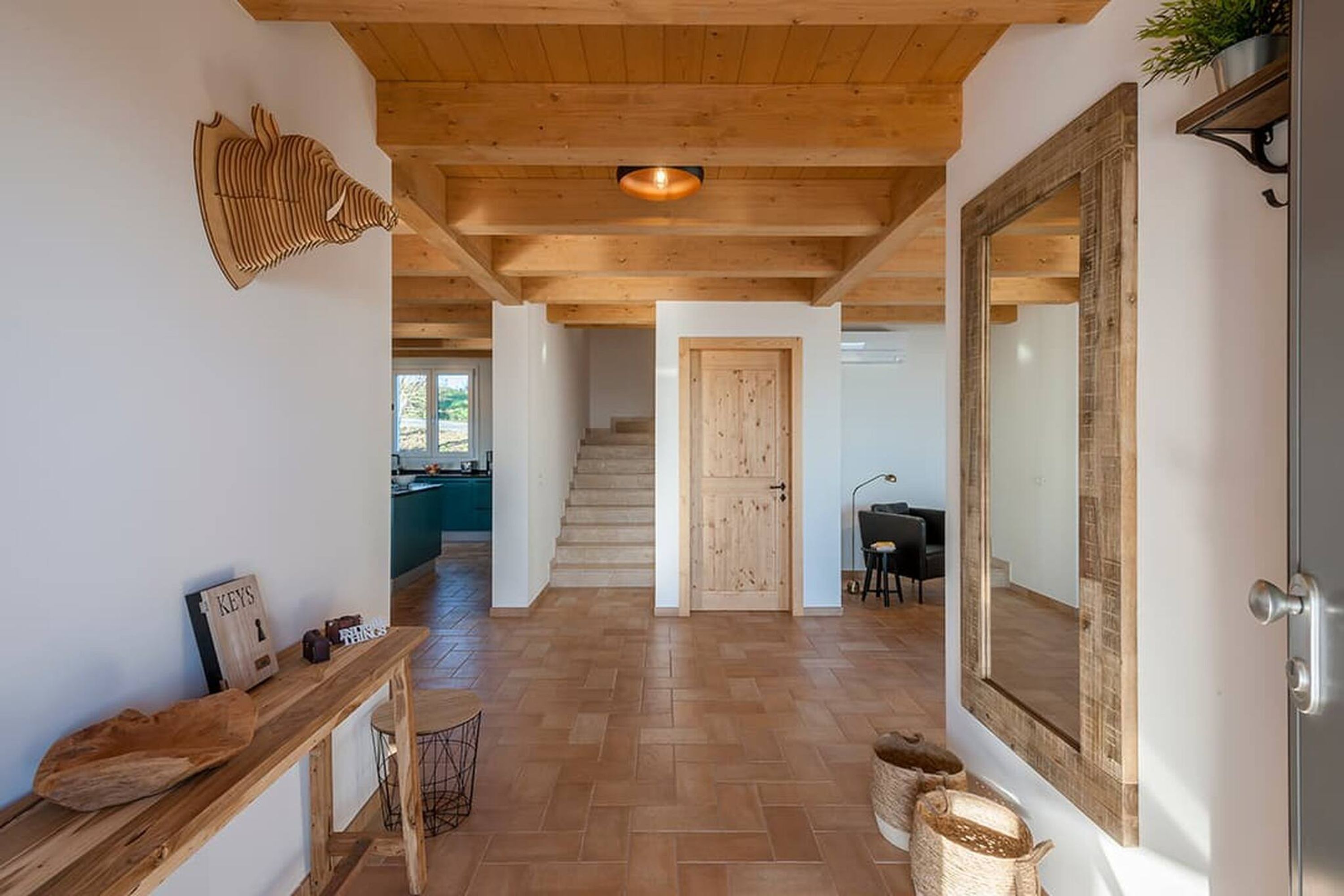 A wooden-floored hallway with a staircase, a wooden bench, and a mirror on the wall.