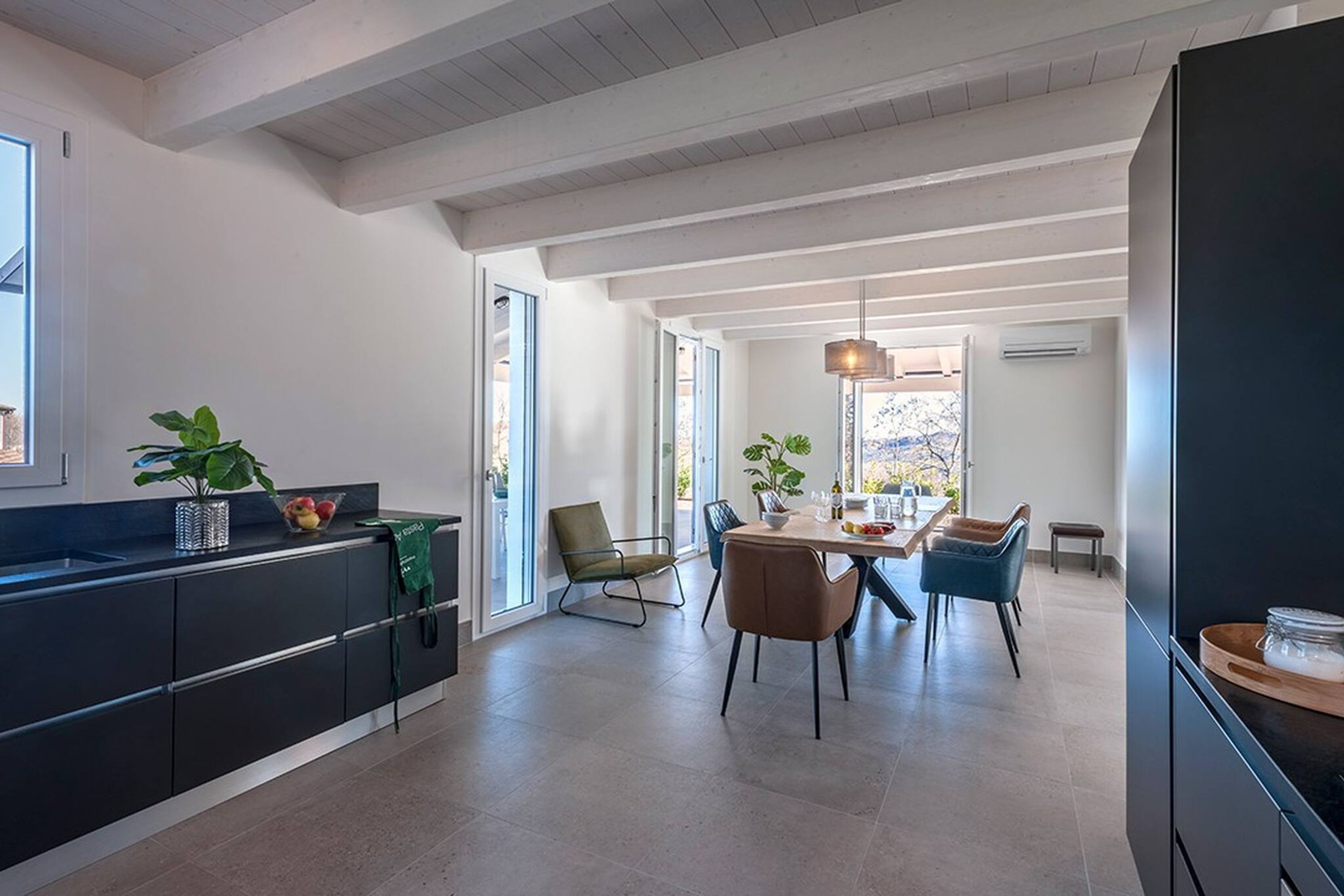 A modern kitchen with dark cabinetry, a dining area with a table and chairs, and large windows allowing natural light.