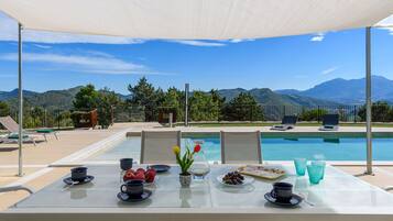 A poolside table with a view of mountains, a pool, and lounge chairs.