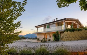 Ein modernes, zweistöckiges Haus mit Balkon, Auffahrt und Blick auf Berge im Hintergrund.