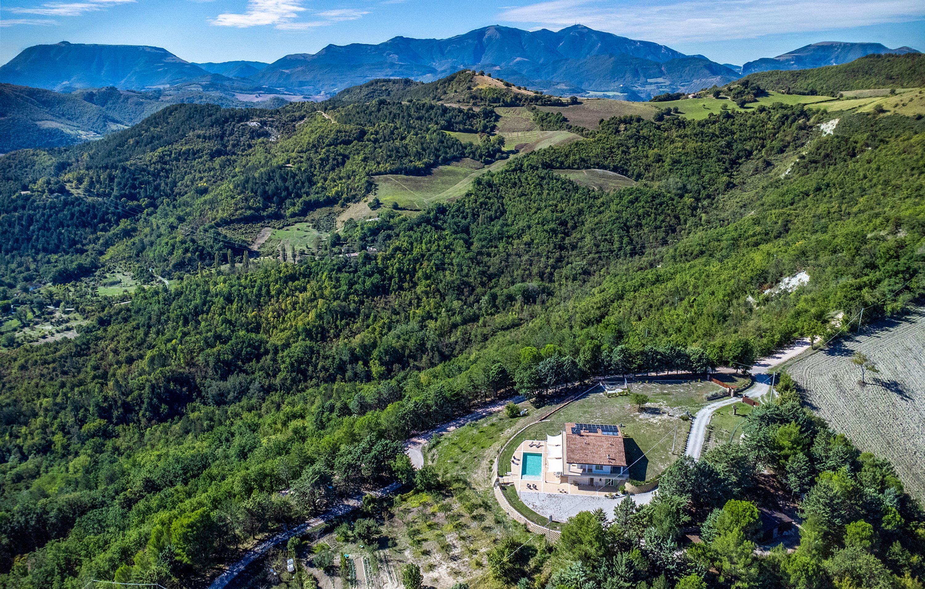 A house with a swimming pool, surrounded by lush green hills and mountains.