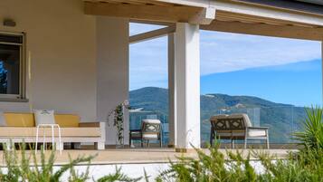 A balcony with a sofa and chairs, overlooking a mountainous landscape.