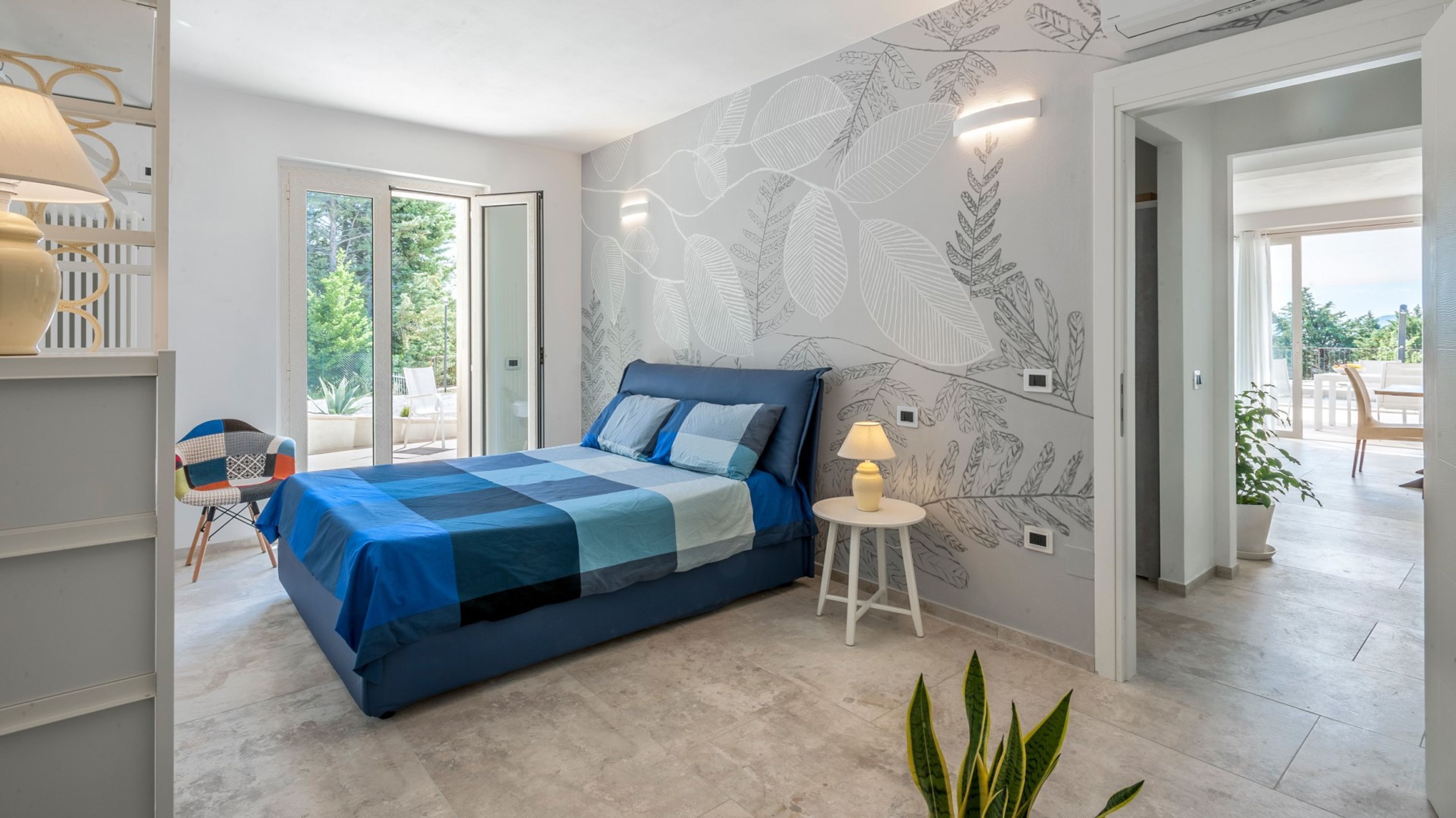 A bedroom with a bed, a chair, a lamp, and a plant.