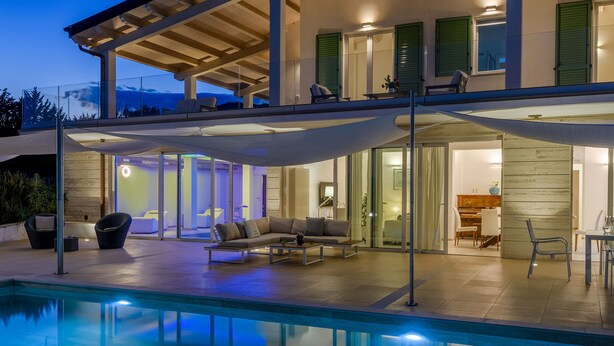 Una casa moderna con piscina, mobiliario exterior y un patio cubierto.