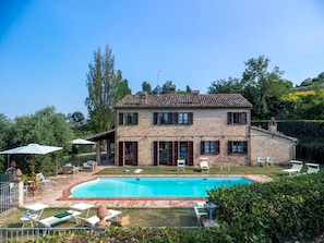 Una casa de piedra de dos pisos con piscina, mobiliario exterior y un jardín bien cuidado.