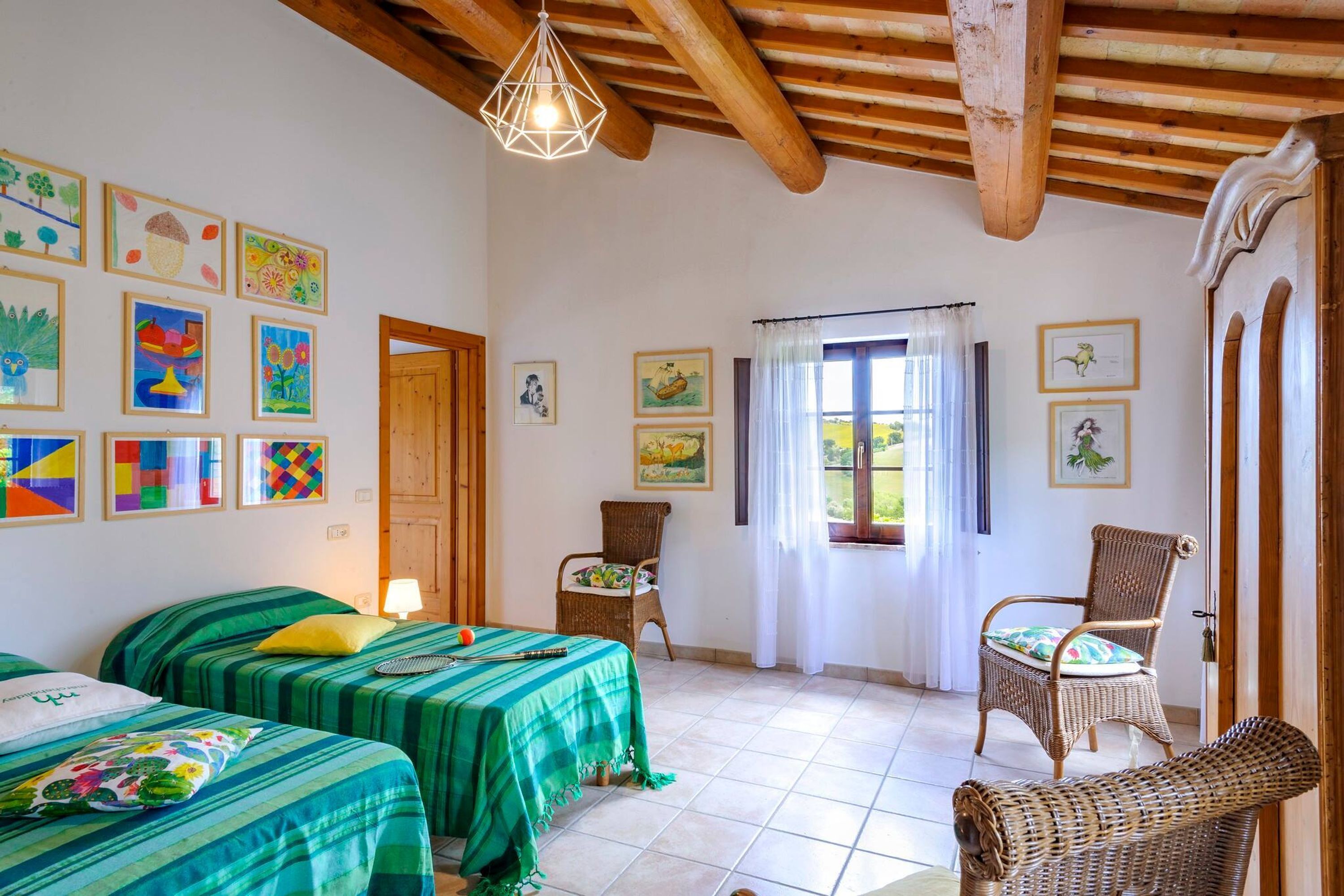A room with two beds, a wicker chair, and various artworks on the walls.