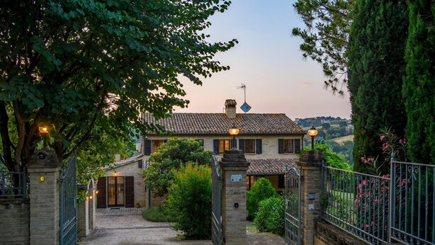 A traditional stone building with a tiled roof, a gated entrance, and a view of a hilly landscape in the background. - La Girolima 6 2 in Mondavio (Mondavio)