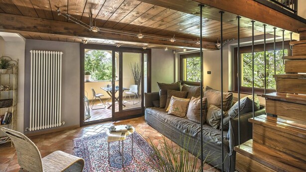 A modern living room with a wooden ceiling, a sofa with cushions, a coffee table, and a view through large glass doors to an outdoor patio. - Casale Degli Ulivi 8 2 (Acqualagna)