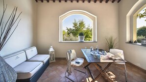 A cozy patio area with a cushioned bench, a dining table set with plates and glasses, and a large arched window offering a view of greenery. - Casale Degli Ulivi 8 2 (Acqualagna)