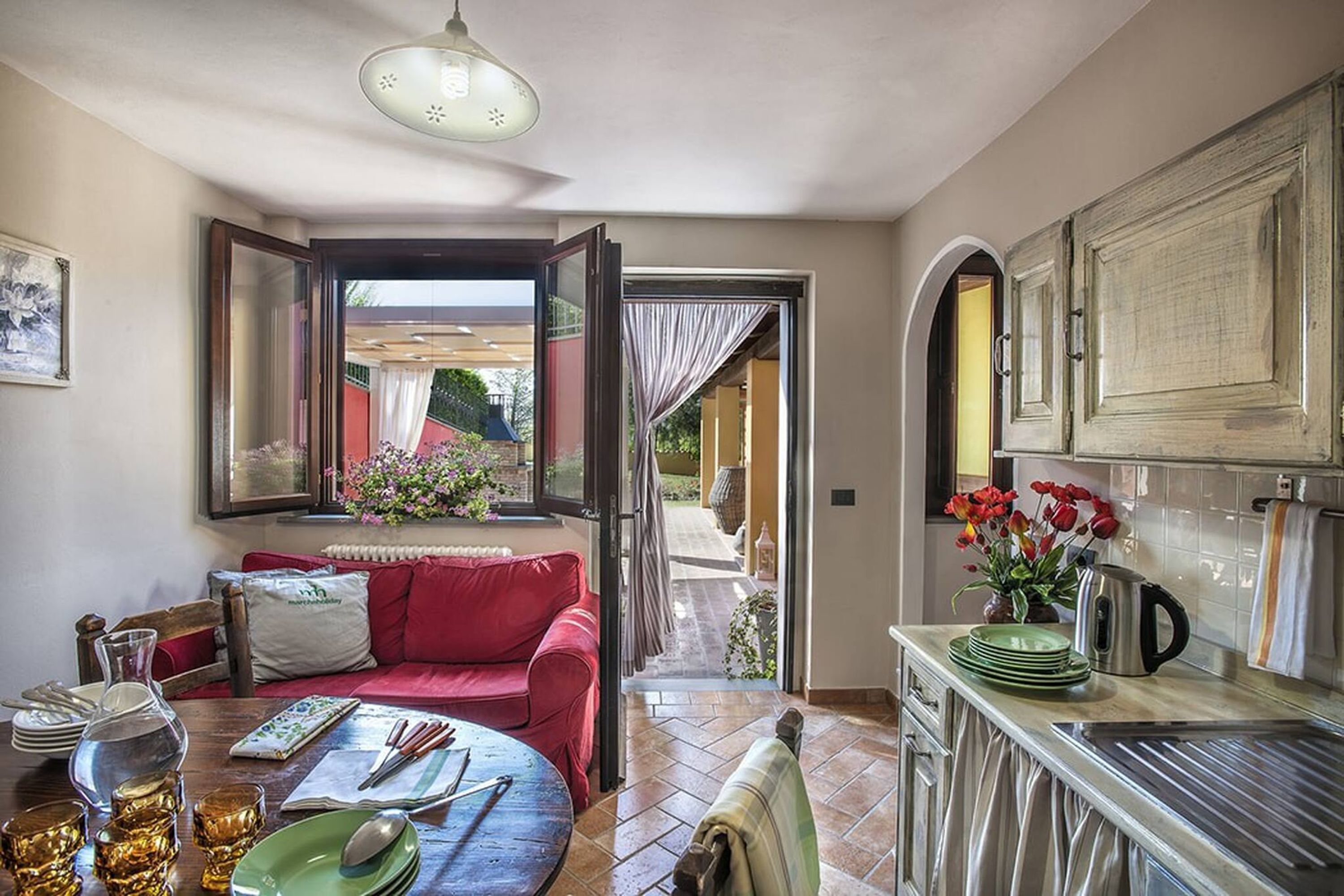 Una sala de estar acogedora con un sofá rojo, una mesa de comedor y una cocina con armarios y encimera.