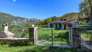 Une maison avec un portail en pierre, un chemin pavé et une vue sur les montagnes en arrière-plan.