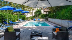 Un espace piscine agrémenté de parasols bleus, de chaises longues et d’une table avec des verres et des tasses.