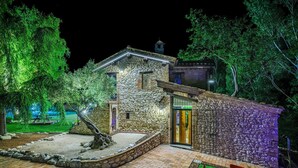 A stone building with a door, surrounded by a garden with a tree and a small patio area with two chairs. - Casalino Galassi 4 2 (Sarnano)