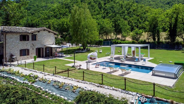 A stone house with a pool, outdoor seating, and a view of a forested hill. - Casalino Galassi 4 2 (Sarnano)