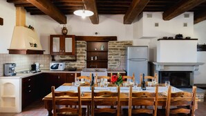 Une cuisine rustique avec des poutres en bois, un mur en pierre, une table à manger dressée pour quatre personnes et une cheminée.