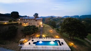 Une maison en pierre avec une piscine, entourée de collines et d’arbres.