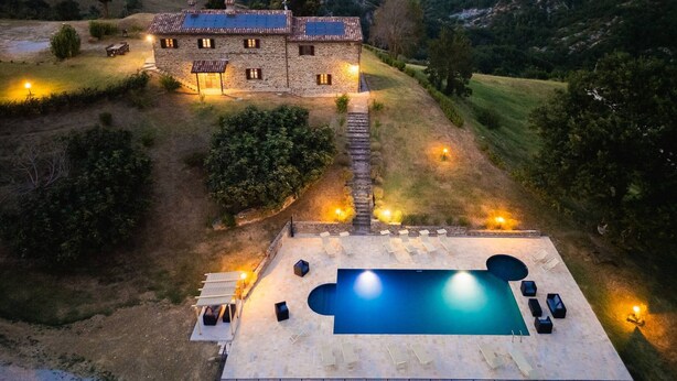 Une maison en pierre avec une piscine, entourée d’un jardin et de collines.