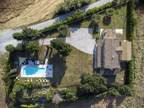 Vista aérea de uma propriedade com piscina, espreguiçadeiras e um edifício com telhado de azulejos.
