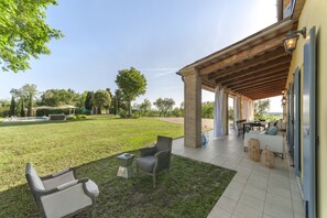 A covered outdoor seating area with a pool, a grassy lawn, and a patio with a table and chairs. - Villa Elettra 12 2 in San Costanzo (San Costanzo)
