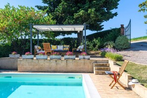 Ein Poolbereich mit einer Pergola, Liegestühlen und einer Holzterrasse.