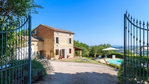A two-story house with a gravel driveway, a swimming pool, and a metal gate. - Casa Felicit 8 in Ripe San Ginesio (Ripe San Ginesio)
