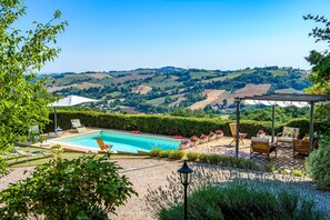 A pool with lounge chairs, a pergola, and a view of rolling hills. - Casa Felicit 8 in Ripe San Ginesio (Ripe San Ginesio)