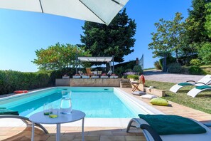 Ein Swimmingpool mit Liegestühlen und einem Tisch, umgeben von Grünflächen und einer Pergola.