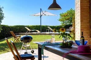 Eine Terrasse im Freien mit Grill, Liegestühlen und einem Tisch mit Getränken und Sonnenblumen.