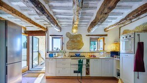 A kitchen with exposed wooden beams, a stone accent wall, a built-in oven, and a refrigerator. - Casa Felicit 8 in Ripe San Ginesio (Ripe San Ginesio)