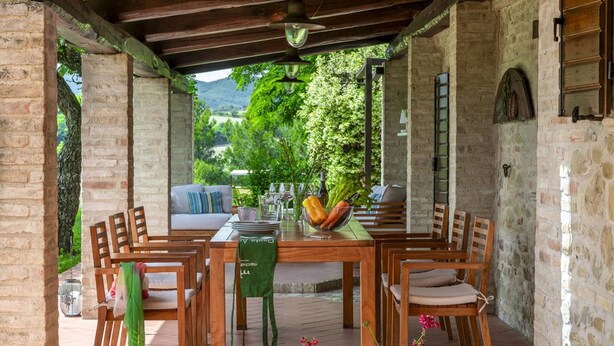 An outdoor dining area with a wooden table and chairs, surrounded by stone walls and greenery. - Casale Belvedere 8 1 by Marche Holiday Villas (Pesaro)