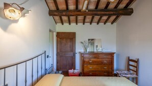 A bedroom with a bed, wooden dresser, and a chair. - Casale Belvedere 8 1 by Marche Holiday Villas (Pesaro)