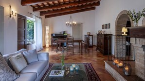 A spacious living room with a wooden ceiling, a fireplace, a dining area, and a sofa with a magazine on the coffee table. - Casale Belvedere 8 1 by Marche Holiday Villas (Pesaro)