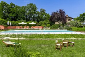 Ein Schwimmbecken mit Liegestühlen und Sonnenschirmen, umgeben von Grünpflanzen und einer Steinmauer.