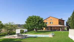 Una casa con piscina, patio coperto e prato.