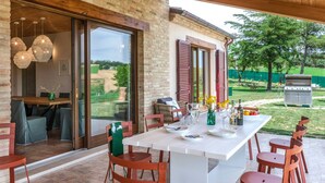 An outdoor dining area with a white table and red chairs, a brick wall, and a view of the garden. - I Gelsi 12 2 in Orciano di Pesaro (Terre Roveresche)