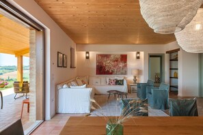 Un salon moderne avec un plafond en bois, une grande peinture abstraite et un coin repas avec des chaises bleues.