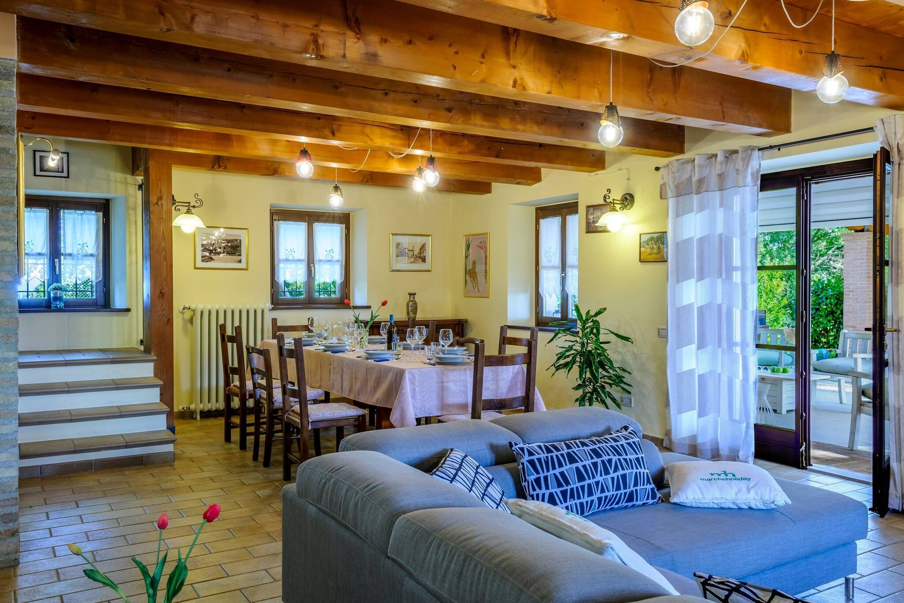 A cozy dining area with a wooden ceiling, a dining table set for four, and a sofa with cushions.