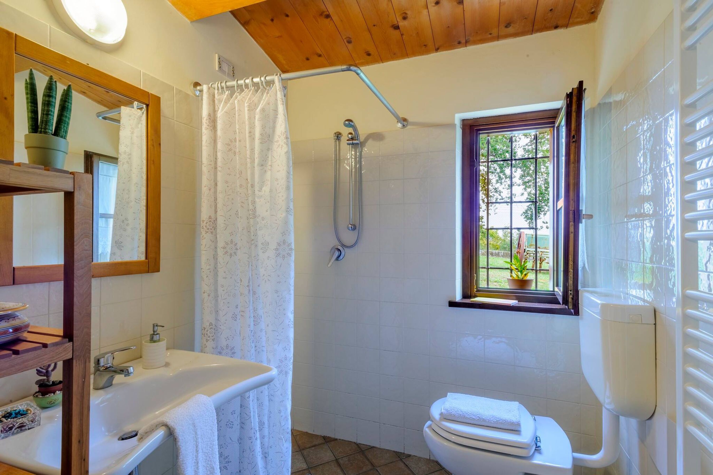 A bathroom with a shower, toilet, sink, and a window with a view of greenery.