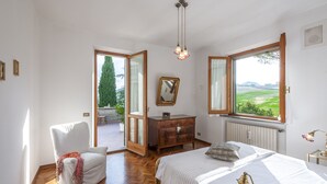 A bedroom with a large window, a wooden dresser, a chair, and a bed. - Villa Paola 10 by Marche Holiday Villas (Sant'Angelo in Vado)