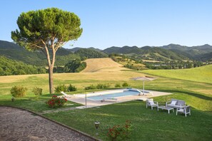 A pool area with lounge chairs and a table, surrounded by a well-maintained lawn and a large tree.