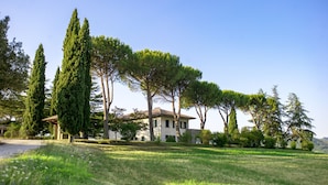 A villa with a large lawn, tall trees, and a clear blue sky. - Villa Paola 10 by Marche Holiday Villas (Sant'Angelo in Vado)