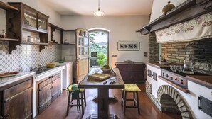 A kitchen with a central island, wooden cabinets, and a brick fireplace. - Villa Paola 10 by Marche Holiday Villas (Sant'Angelo in Vado)