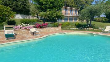 A swimming pool with two lounge chairs, surrounded by a stone patio and lush greenery.
