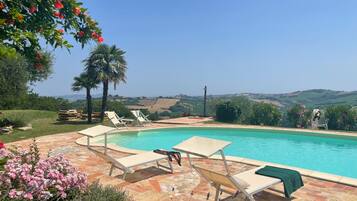A pool area with lounge chairs, a stone patio, and a view of the countryside.