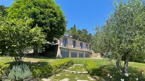 A house with a stone pathway leading to a garage, surrounded by well-maintained lawns and various shrubs. - Casa Zefiro 4 in Orciano di Pesaro (Terre Roveresche)