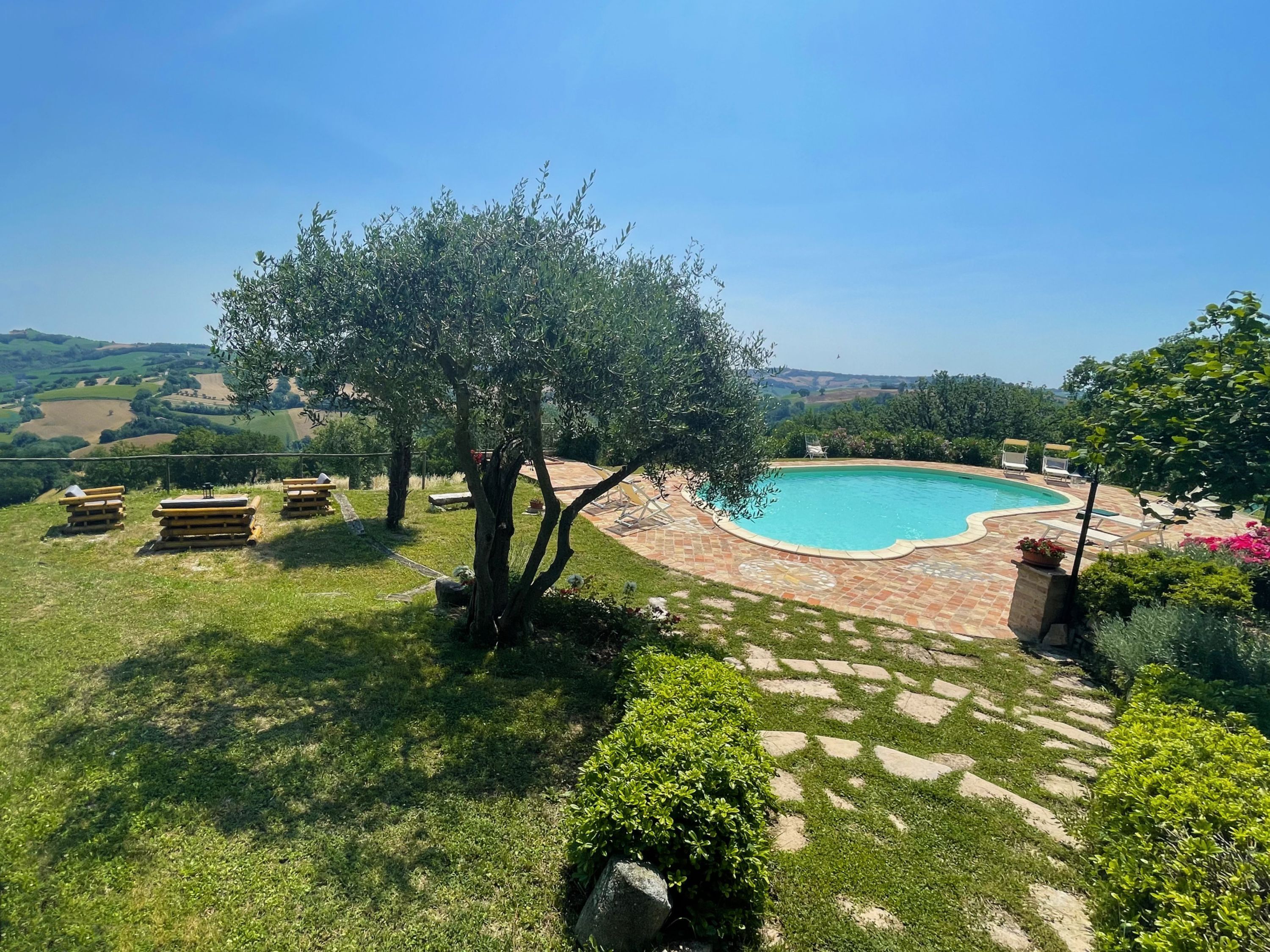 Zona de piscina con vista despejada del paisaje circundante, incluyendo un árbol y una zona cubierta de césped.