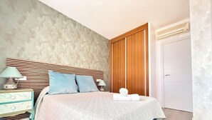 Ein Schlafzimmer mit einem Bett, zwei Kissen, einem Nachttisch mit Lampe, einem Holzschrank und einer weißen Tür.